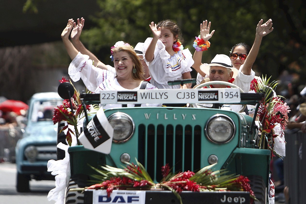 Una familia saluda a asistentes del tradicional desfile de autos clásicos y antiguos durante la Feria de las Flores.