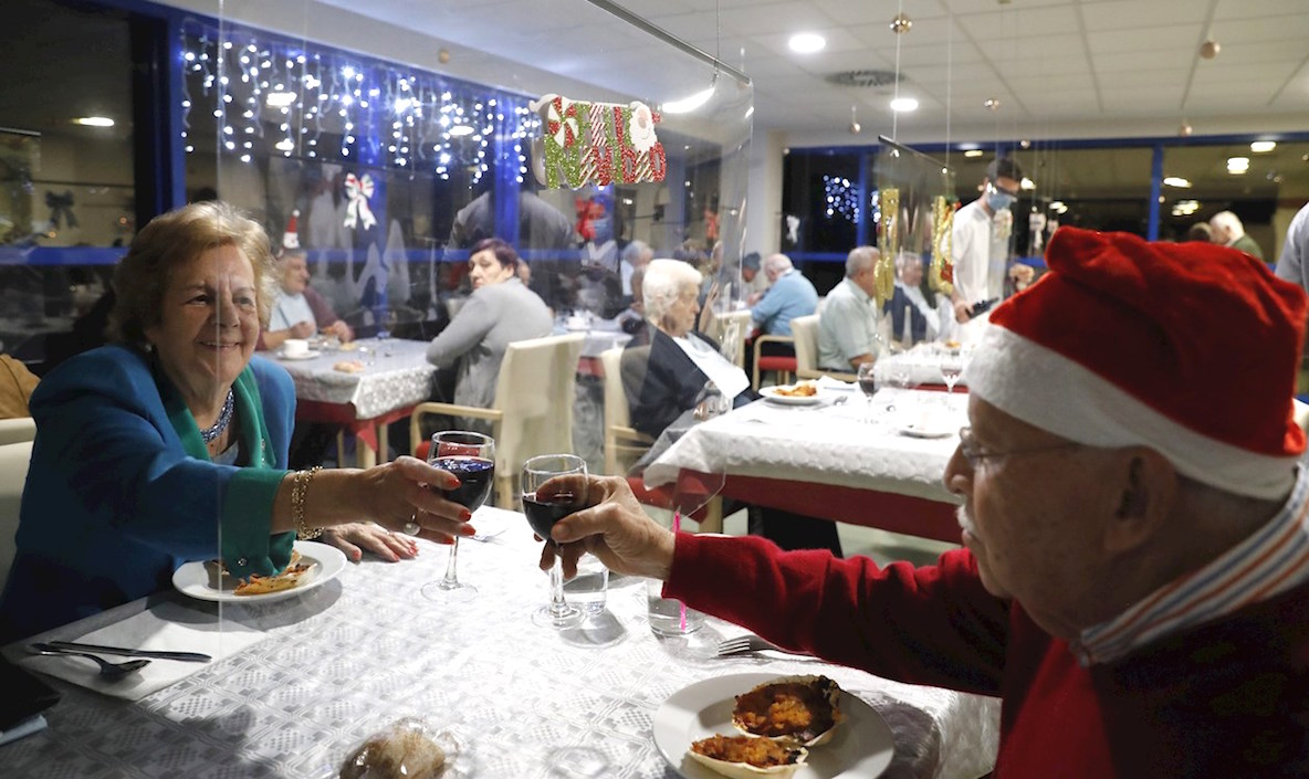 Adultos mayores residentes del centro Domus VI San Lázaro celebran durante la cena de Nochebuena con un menú especial y en mesas con mamparas, en Santiago de Compostela, España.
