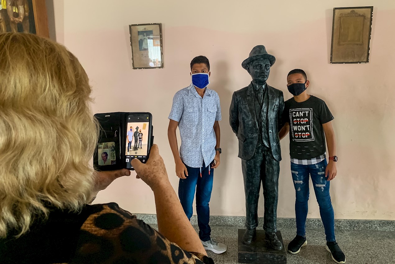 Una mujer tomar una foto a dos jóvenes junto a una estatua de José Gregorio Hernández, en Isnotú (Venezuela).