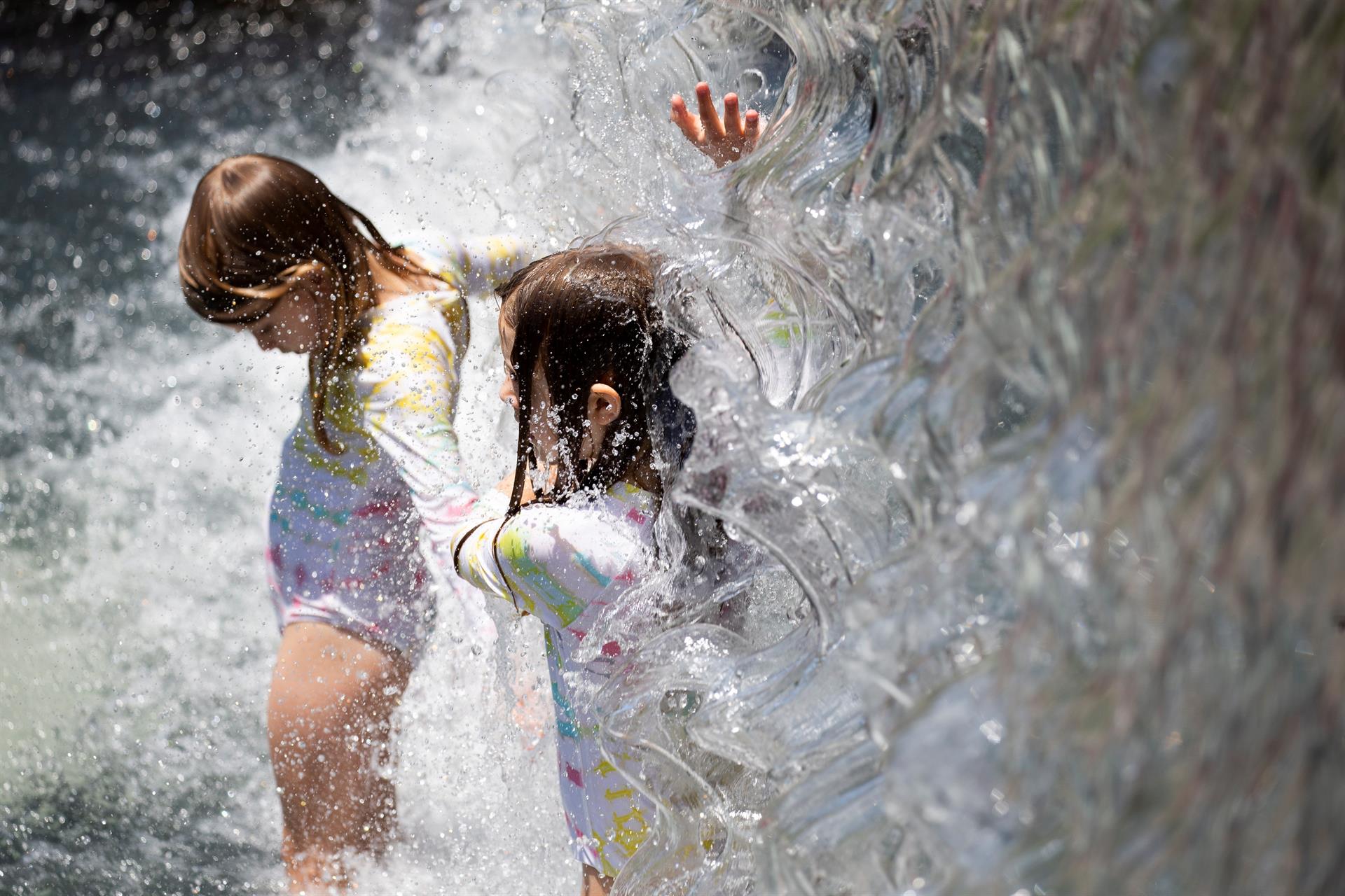 Los niños pasan a través de una cascada en un parque durante el clima cálido y húmedo en Washington