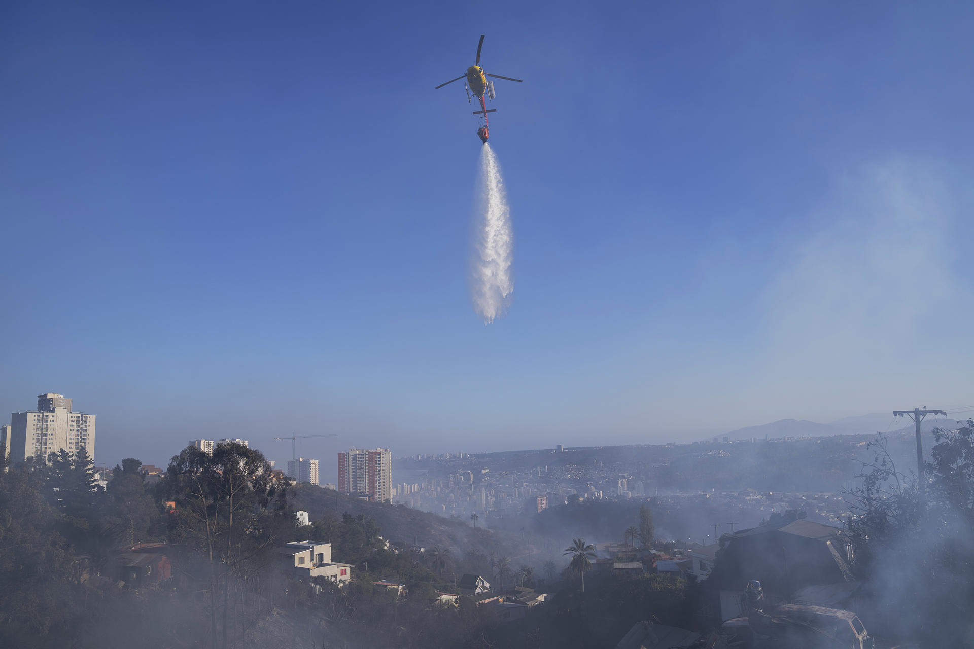 Un helicóptero descarga agua durante los trabajos para apagar un incendio hoy, en cerro Forestal, en Viña del Mar