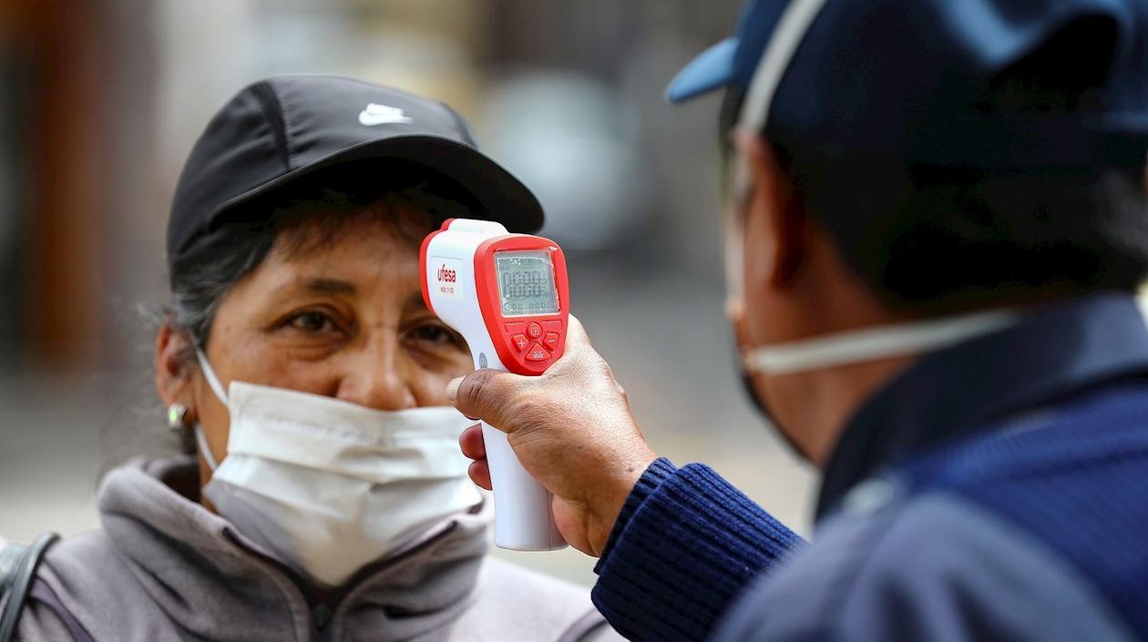 Una mujer con tapabocas le miden la temperatura antes subir a un transporte público.