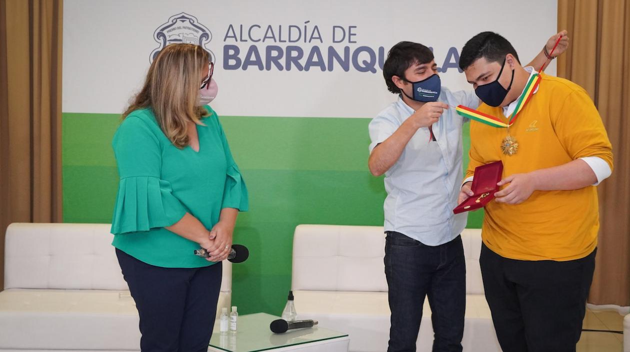 Alcalde Pumarejo condecora al estudiante Alejandro Salas por su puntaje perfecto de las Pruebas Saber 11. Observa la secretaria de educación, Bibiana Rincón.