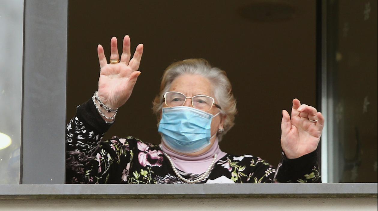 Una señora saluda desde su ventana en una residencia de ancianos. 