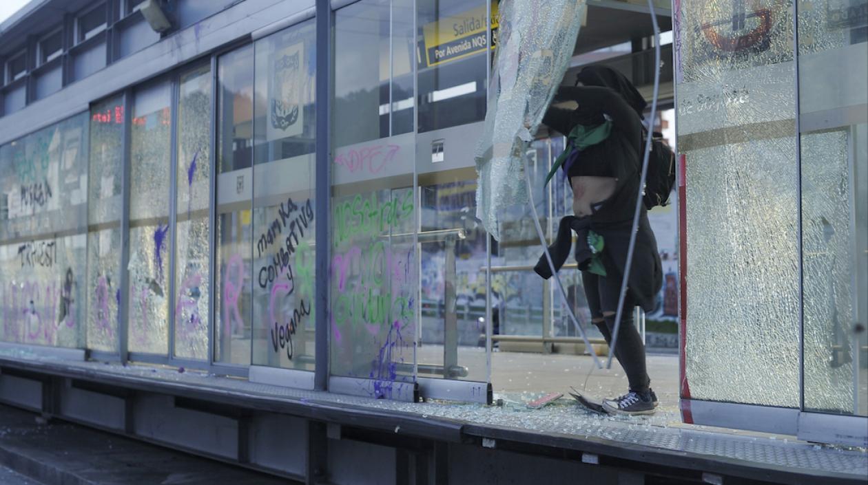 Una mujer rompiendo los vidrios en una estación de Transmilenio durante la marcha en Bogotá.