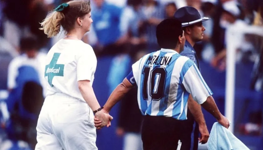 Diego Maradona sale de la mano con una voluntaria de la FIFA que lo conduce al examen antidoping. 