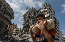 Un palestino lleva pan y al fondo se ven edificios destruidos en la ciudad de Gaza.