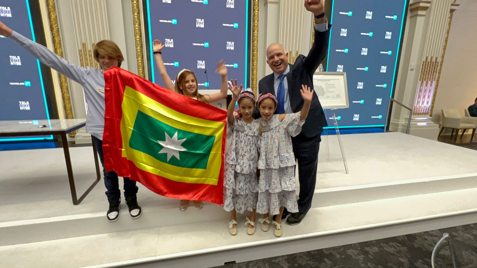 El COO de Tecnoglass, Christian Daes, con sus hijos y niños que acompañaron a la delegación, portando la bandera de Barranquilla, en la Bolsa de Valores de Nueva York, donde tocaron la campana.