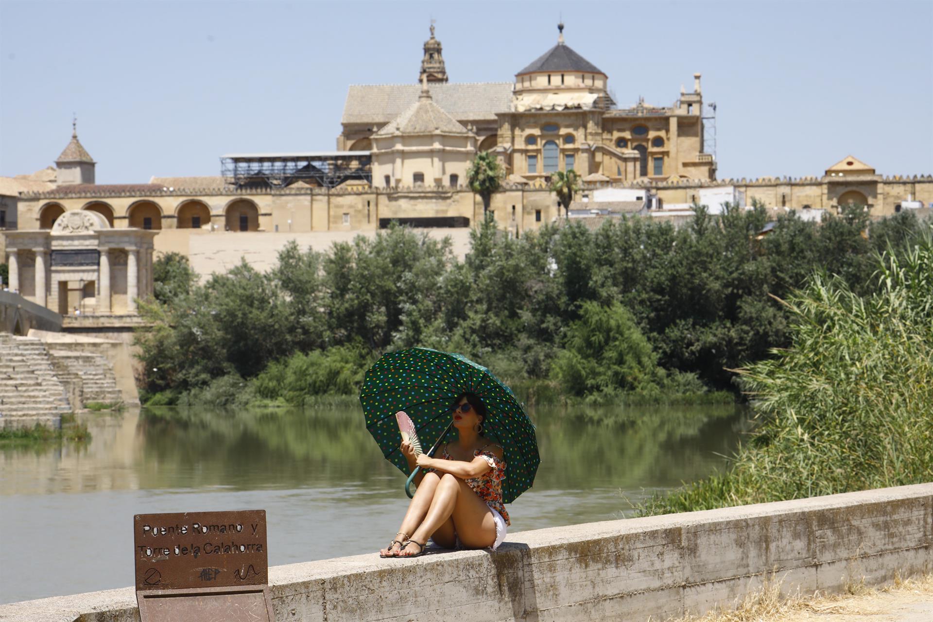 Una turista se protege del calor con un paraguas y un abanico a la orilla del río Guadalquivir cerca de la Mezquita-Catedral de Córdoba