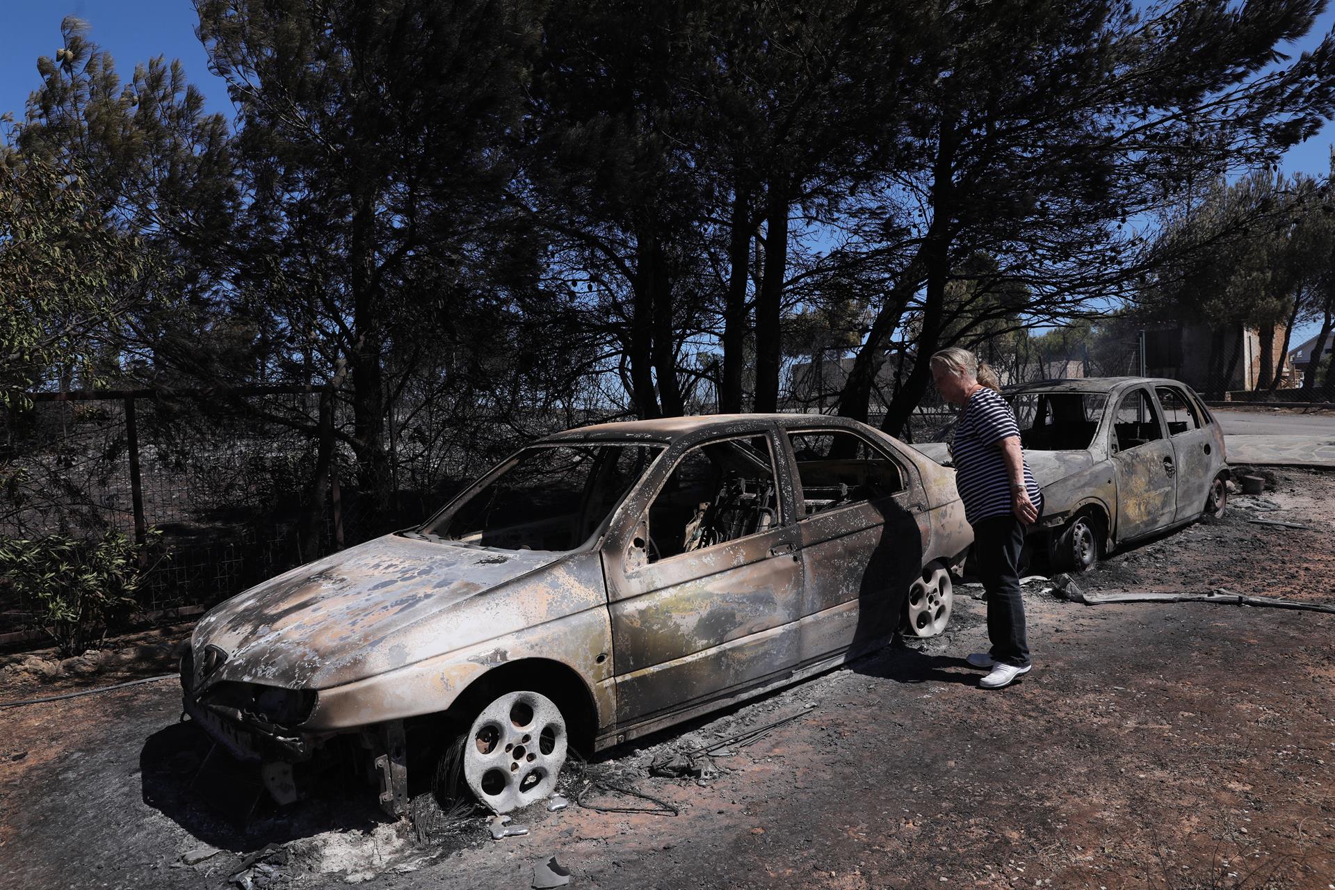 Una mujer observa los coches quemados del incendio acaecido en Anthousa, cerca de Atenas, Grecia.