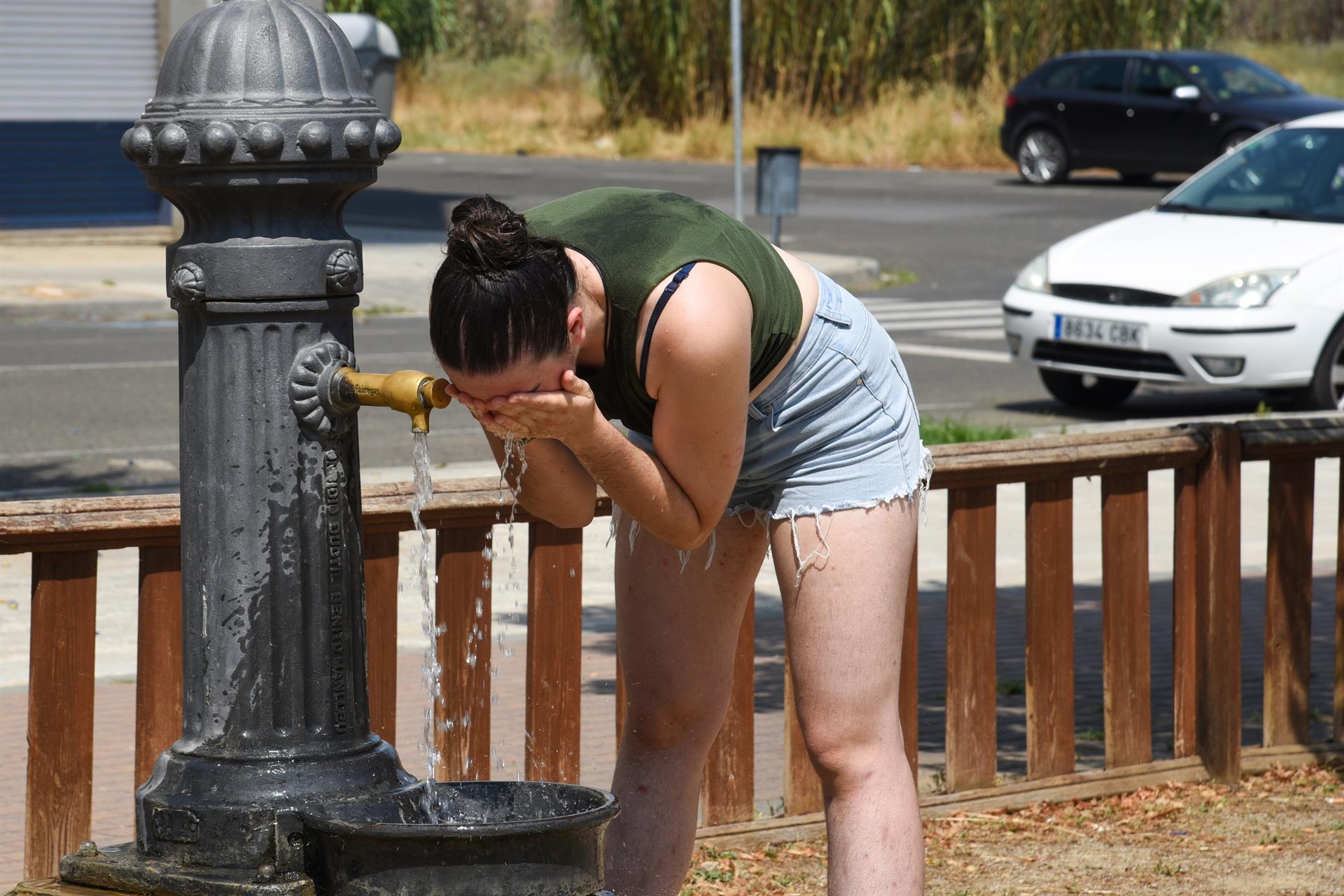 Una joven se refresca en un fuente de un parque de Lleida, España, por el intenso calor.