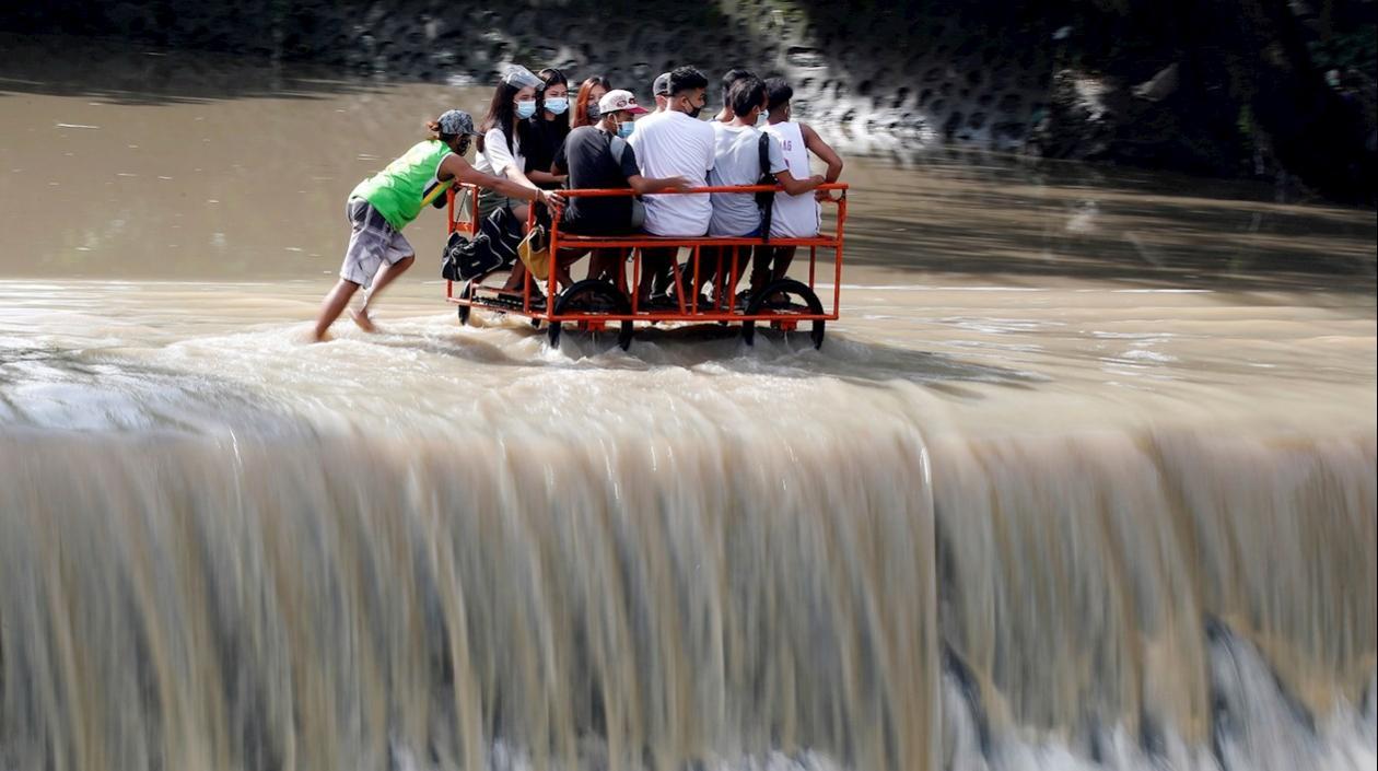 Varios lugareños cruzan en una carreta una presa desbordada en la frontera entre la provincia de Cavite y la ciudad de Las Piñas, en Filipinas, este domingo.