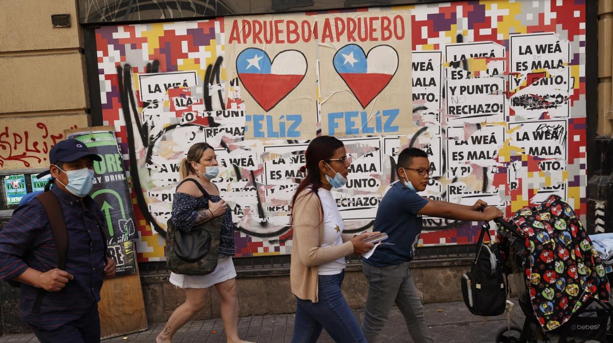 Varias personas caminan frente a una pared con información relacionada al plebiscito constitucional del domingo en Chile.