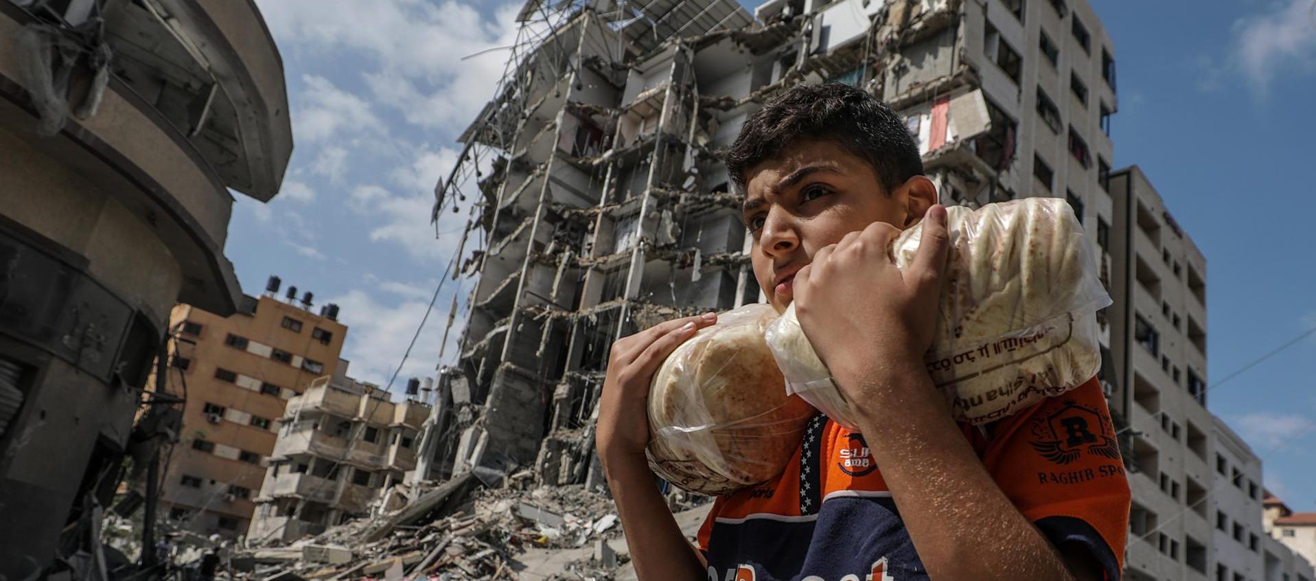 Un palestino lleva pan y al fondo se ven edificios destruidos en la ciudad de Gaza.
