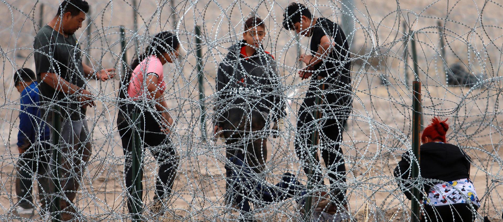 Migrantes intentan cruzar la cerca de alambres en la frontera que divide a México de los Estados Unidos. 