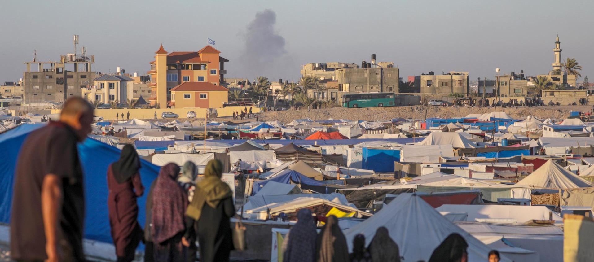Desplazados internos palestinos y al fondo tras un ataque aéreo israelí en Rafah.