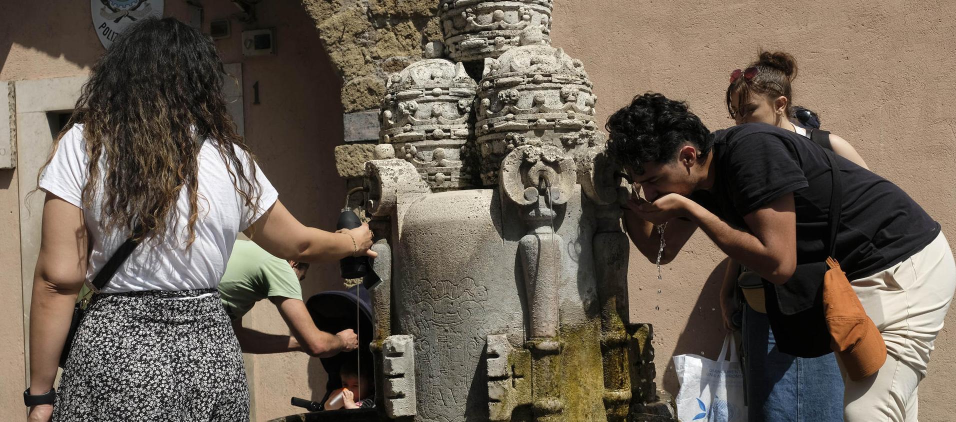 Varias personas se refrescan en una fuente en Roma, Italia.