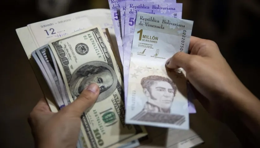 Una persona sostiene un fajo de billetes de dólares y bolívares.