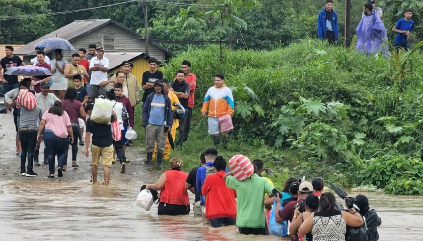 Comunidad cruzando con sus pertenencias por un río en medio de las inundaciones.