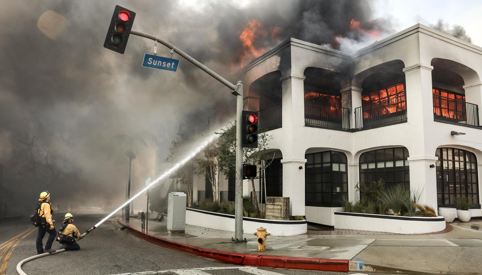 Los bomberos luchan contra las llamas que envuelven un edificio durante el incendio forestal de Palisades. 