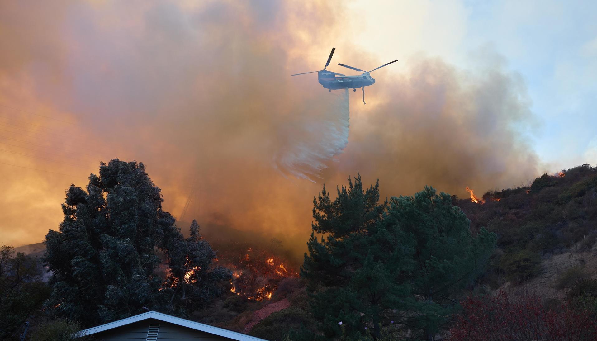 Un helicóptero arroja agua sobre una casa durante el incendio forestal en Los Ángeles.