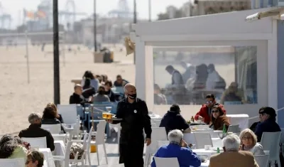 Un camarero atiende las mesas de una terraza en un restaurante en la playa.