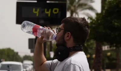 Un ciudadano bebe agua con el fondo de un termómetro que marca 44 grados.
