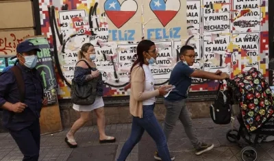 Varias personas caminan frente a una pared con información relacionada al plebiscito constitucional del domingo en Chile.