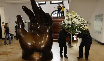 Empleados dejan un arreglo floral junto a la escultura La Mano de Fernando Botero.