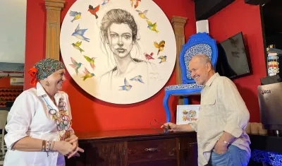 Carla Celia y Joaquín Botero frente a una pintura y una silla restaurada que hacen parte de la exposición de arte de Nonna Rosa